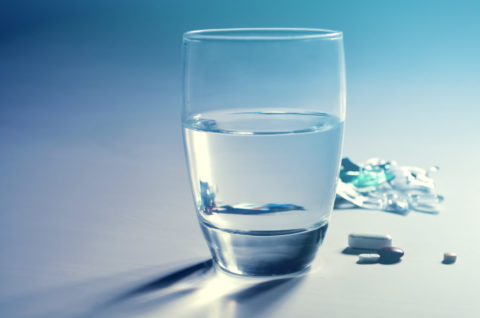 A half-full glass of water and a few pills next to it.