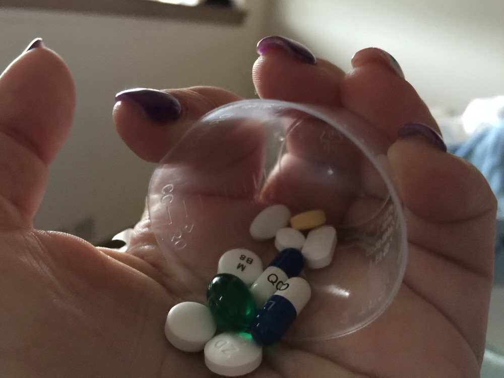 A woman's hand holding a cup full of pills